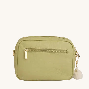 Green crossbody bag with a gold zipper and white pom-pom on a light gray background