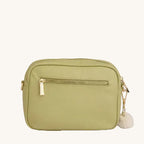 Green crossbody bag with a gold zipper and white pom-pom on a light gray background