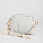 Light grey crossbody bag with a patterned strap on a light gray background