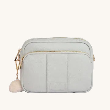 Light gray crossbody bag with gold zipper and white pom-pom on a light gray background