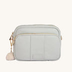 Light gray crossbody bag with gold zipper and white pom-pom on a light gray background