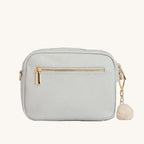 Light grey crossbody bag with gold zipper and pom-pom on a light gray background