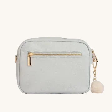 Light grey crossbody bag with gold zipper and pom-pom on a light gray background