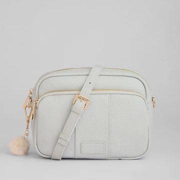 Light gray crossbody bag with a pom-pom detail on a light gray background