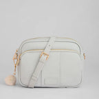 Light gray crossbody bag with a pom-pom detail on a light gray background