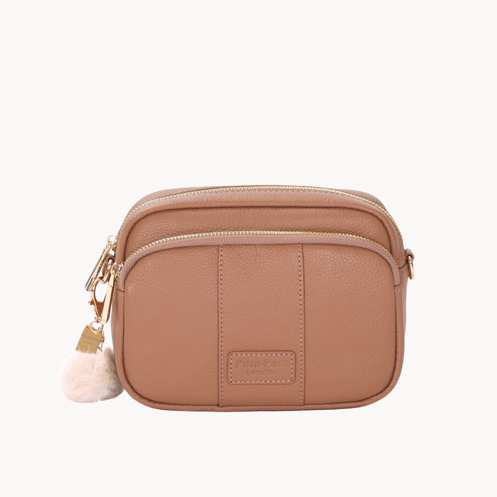 Brown leather crossbody bag with a pom-pom charm on a white background