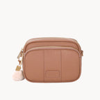 Brown leather crossbody bag with a pom-pom charm on a white background