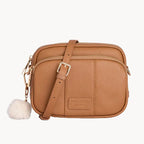 Tan leather crossbody bag with a fluffy pom-pom on a light gray background