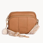 Tan leather crossbody bag with patterned strap on a light gray background