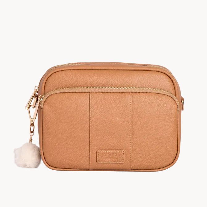 Tan leather crossbody bag with a small white pom-pom on a light gray background