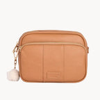 Tan leather crossbody bag with a small white pom-pom on a light gray background