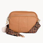 Tan crossbody bag with a patterned strap on a light gray background