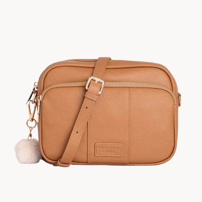 Tan crossbody bag with a fluffy pom-pom charm on a light gray background