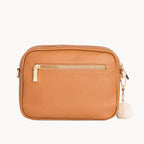 Tan crossbody bag with gold zipper on a light gray background