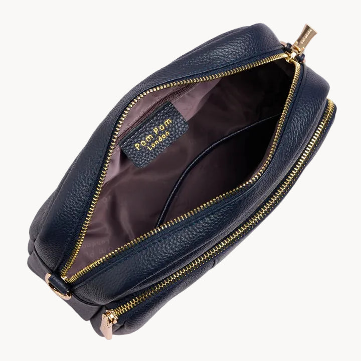 Navy leather crossbody bag with gold zipper on a light gray background