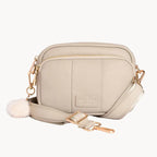 Stone crossbody bag with a pom-pom detail on a light gray background