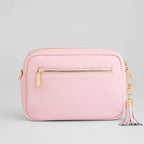 Pink crossbody bag with a gold zipper and tassel on a light gray background