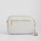 Light gray crossbody bag with a gold zipper and tassel on a light gray background