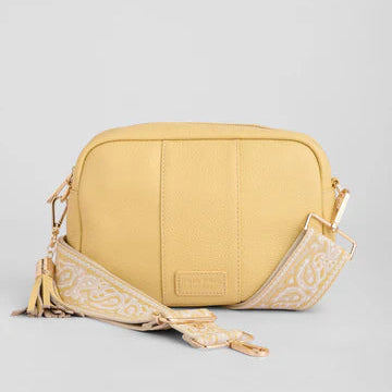 Yellow crossbody bag with a decorative strap on a light gray background