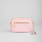Pink crossbody bag with gold zipper and tassel on a light gray background