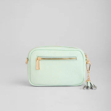 Mint green handbag with a gold zipper and tassel on a light gray background