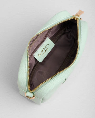 Mint green bag with gold zipper and 'Pom Pom London' label on a light gray background