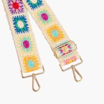 Colorful floral-patterned bag strap with gold hardware on a light gray background