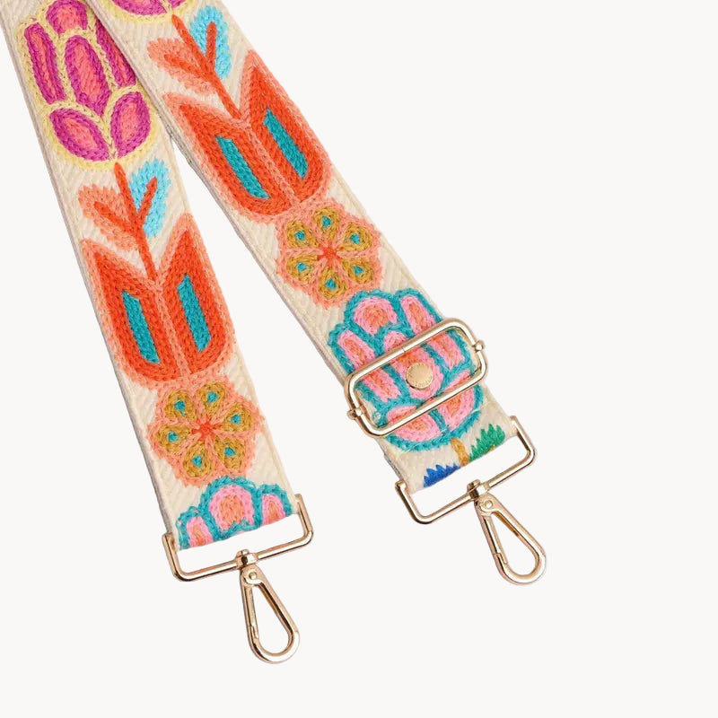 Embroidered floral strap with gold hardware on a light gray background