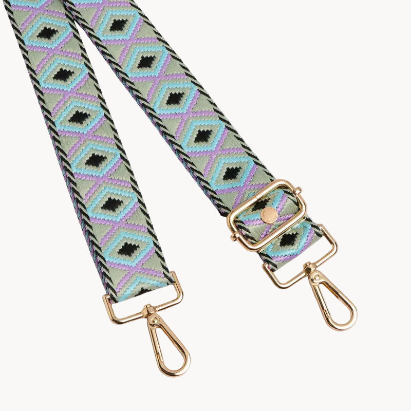 Patterned bag strap with gold hardware on a light gray background