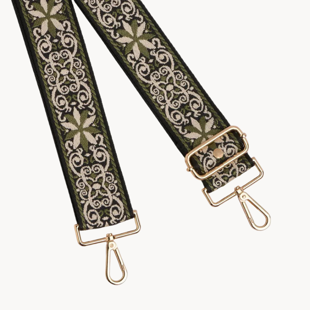 Decorative bag strap with floral pattern and gold hardware on a gray background