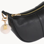 Black leather handbag with gold zipper and decorative keychain on a white background