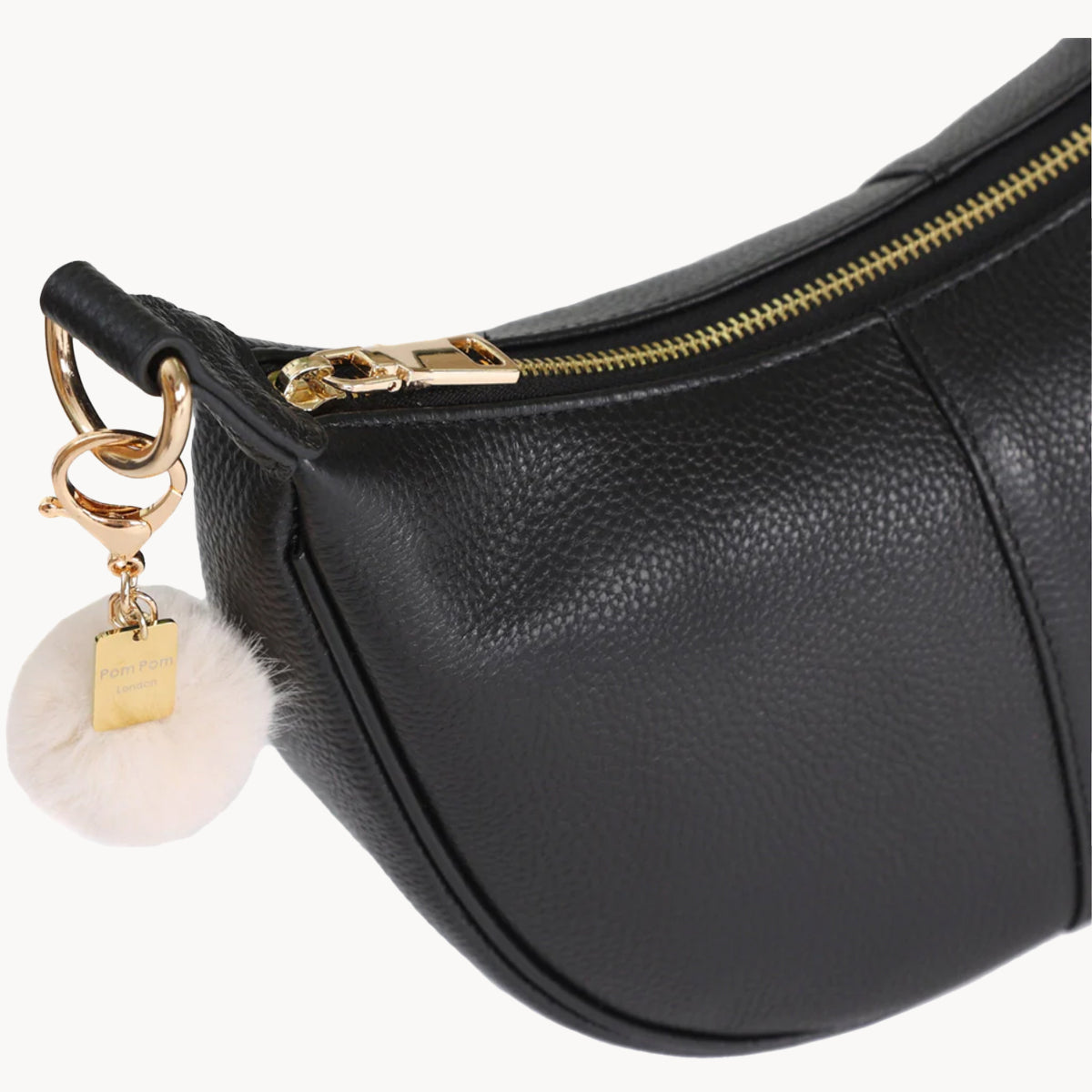 Black leather handbag with gold zipper and decorative keychain on a white background