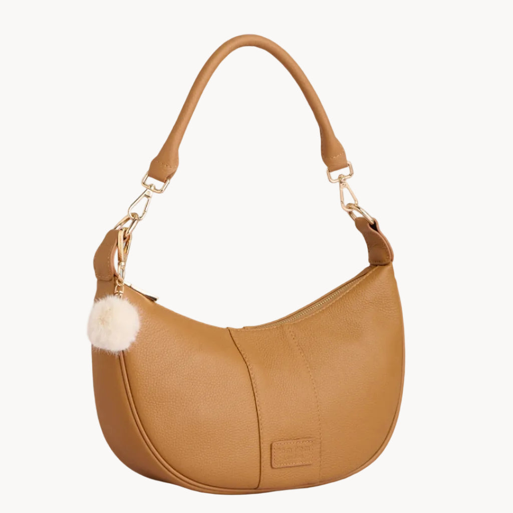 Tan handbag with a fluffy pom-pom on a light gray background