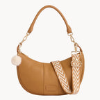 Tan handbag with a decorative strap on a gray background