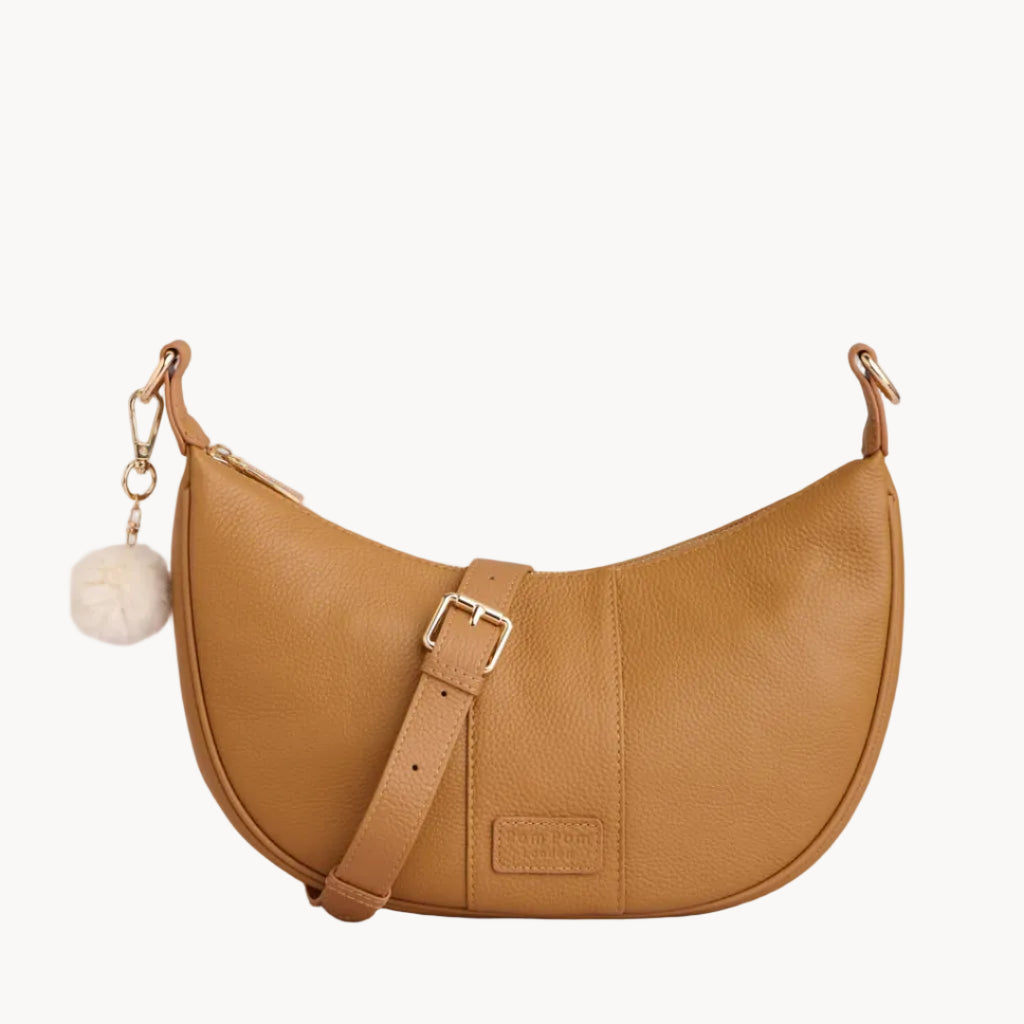 Tan handbag with a strap and decorative element on a light gray background