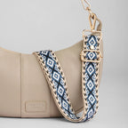 Tan handbag with a blue and white patterned strap on a gray background